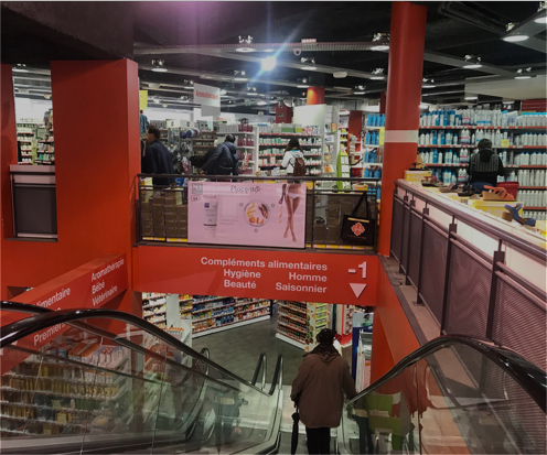 Vue d'une pharmacie sur deux niveaux, avec escalator et rayons de produits de santé et beauté